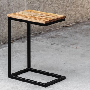 May include: A black metal side table with a rectangular wooden top. The table has a simple, modern design and is perfect for a small space.