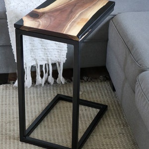 May include: A black metal side table with a live edge walnut wood top and black epoxy resin inlay. The table is sitting on a gray rug.