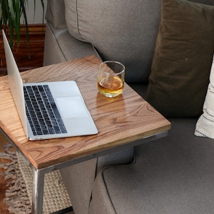 May include: A wooden side table with a metal frame sits next to a gray couch. A laptop computer and a glass of amber liquid are on the table.