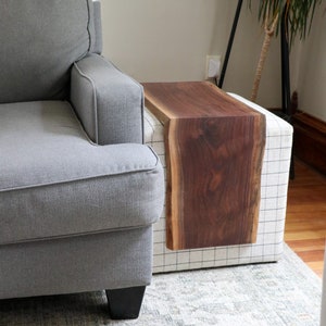May include: A gray upholstered armchair with a black wooden base sits next to a white and black checkered ottoman with a live edge walnut wood top.
