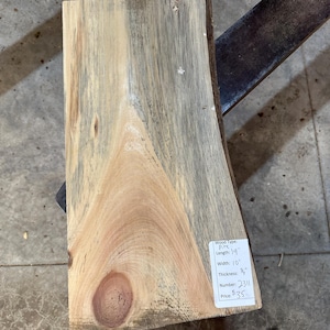 May include: A rectangular piece of pine wood with a natural grain pattern. The wood is approximately 19 inches long, 10 inches wide, and 0.75 inches thick. A label on the wood indicates the wood type, dimensions, and a number.