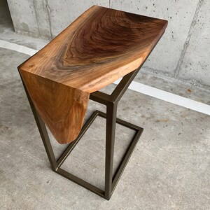 May include: A dark brown wooden side table with a unique, organic shape and a metal frame. The table has a natural, live edge design and a brushed gold finish.
