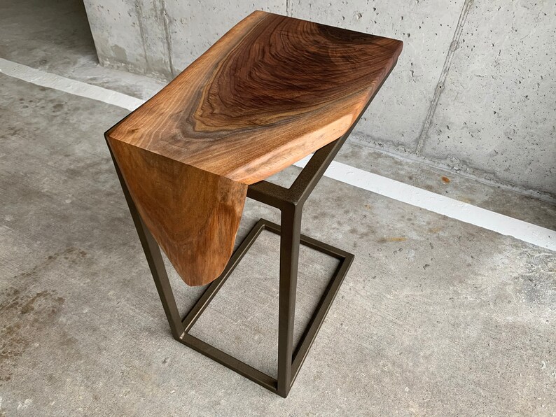 May include: A dark brown wooden side table with a unique, organic shape and a metal frame. The table has a natural, live edge design and a brushed gold finish.