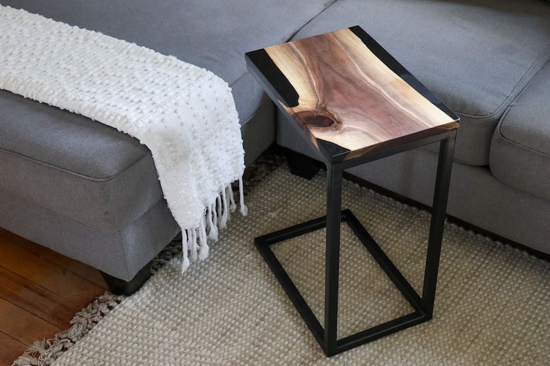 May include: A black metal side table with a wooden top and black epoxy resin inlay. The table has a rectangular top and a square base.