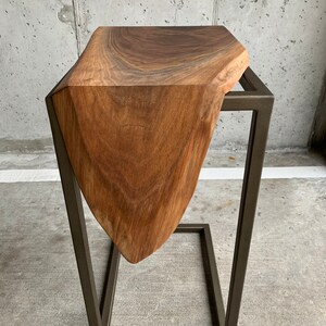 May include: A wooden side table with a unique, organic shape and a dark brown finish. The table is supported by a black metal frame.