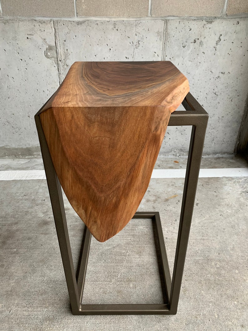 May include: A wooden side table with a unique, organic shape and a dark brown finish. The table is supported by a black metal frame.