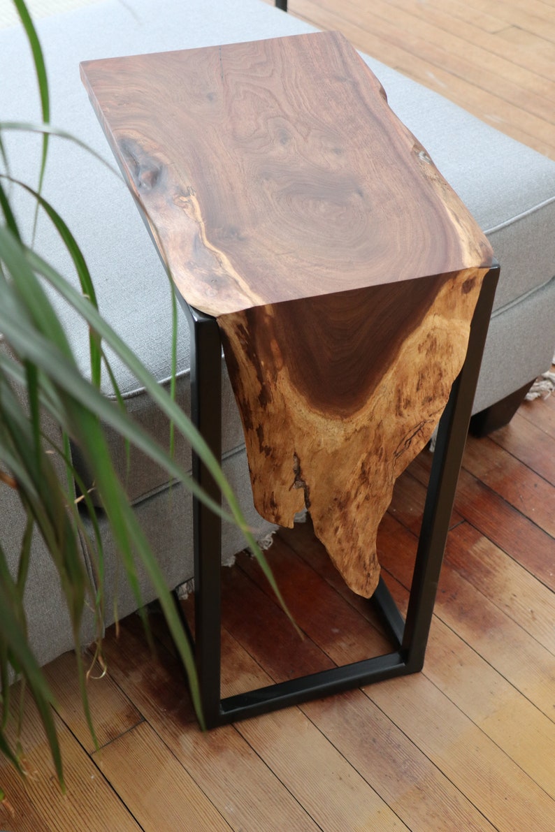 May include: A wooden side table with a live edge top and a black metal frame. The table is made of natural wood with a unique grain pattern.