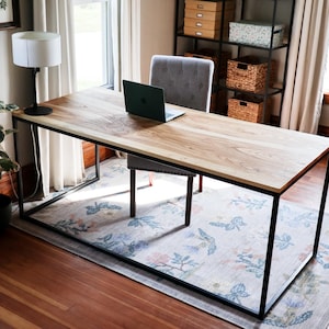 May include: A wooden desk with a black metal frame sits on a patterned rug in a home office. A laptop computer is on the desk, along with a lamp.
