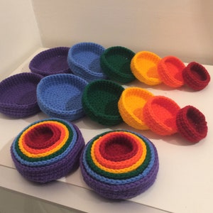 Può includere: Una collezione di ciotole all'uncinetto fatte a mano in varie dimensioni e colori, tra cui viola, blu, verde, giallo, arancione e rosso. Le ciotole sono disposte in un motivo arcobaleno, mostrando le tonalità vivaci e le trame del filato.