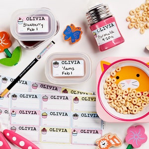 May include: A set of colourful, personalised labels with a cupcake design. The labels feature the name "Olivia" and are designed for use on food containers. The labels are shown on a variety of containers, including a glass jar, a plastic container, and a metal bottle. The labels are also shown on a sheet of stickers.