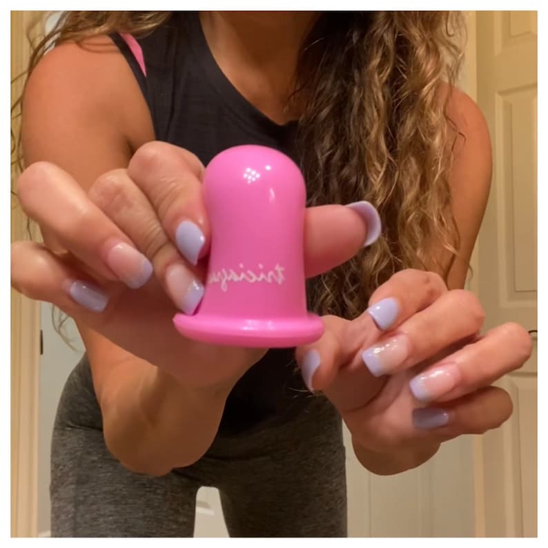 May include: A pink silicone suction cup with the word "against" written on it. The cup is being held by a person with light blue nail polish.
