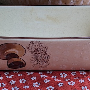 May include: A ceramic loaf pan with a brown rim and a design of brown mushrooms on a beige background.