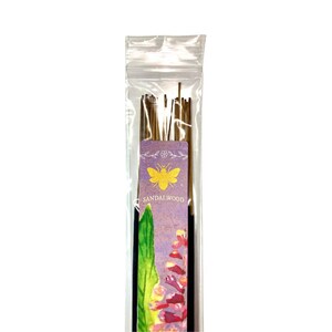 May include: A clear plastic packet of sandalwood incense sticks. The label has a purple background with a yellow bee illustration and the word "Sandalwood". The incense sticks are brown and appear to be made of wood.