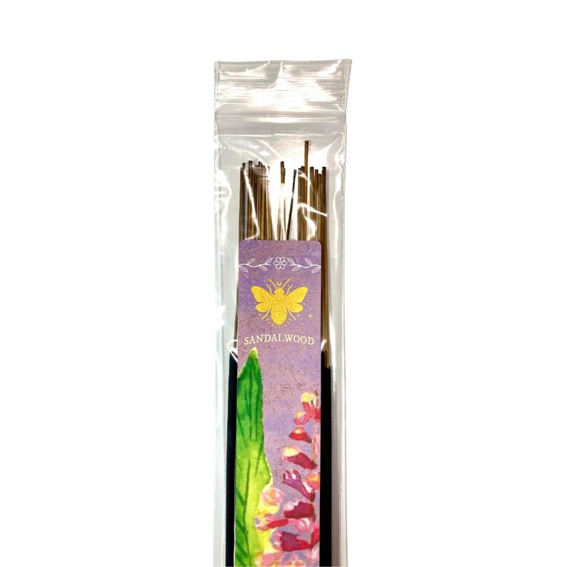 May include: A clear plastic packet of sandalwood incense sticks. The label has a purple background with a yellow bee illustration and the word "Sandalwood". The incense sticks are brown and appear to be made of wood.