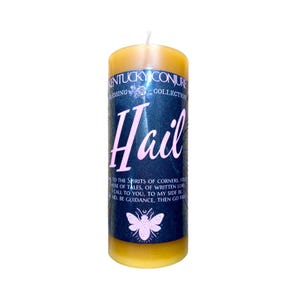 May include: A tall, yellow pillar candle with a white wick. The candle has a dark blue label with the word "Hail" in pink script. The label also includes text and a bee illustration. The candle is part of the "Kentucky Conjure Blessing Collection."