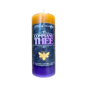 May include: A tall, layered candle with a yellow top, a dark blue middle section, and a purple base. The candle has the text "COMMAND THEE" in purple and gold, with a gold moth graphic. The label also reads "DOUBLE ACTION COLLECTION".