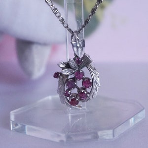May include: A silver necklace with a pendant featuring a cluster of pink gemstones surrounded by silver leaves.