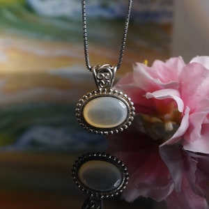 May include: A silver chain necklace with a round, white, iridescent pendant. The pendant has a silver filigree design around the edge.
