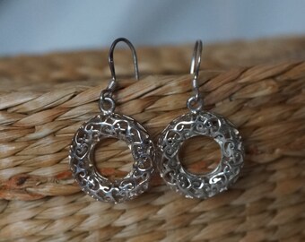 May include: A pair of silver dangle earrings featuring a delicate, circular design. The earrings are crafted from intricate filigree work and have a slightly oxidised finish.
