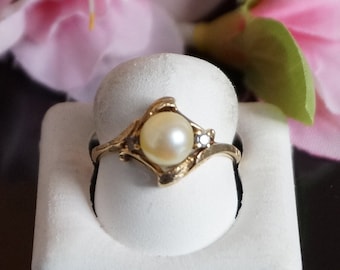 May include: A gold ring with a single pearl and two small diamonds set in a delicate, curved design.