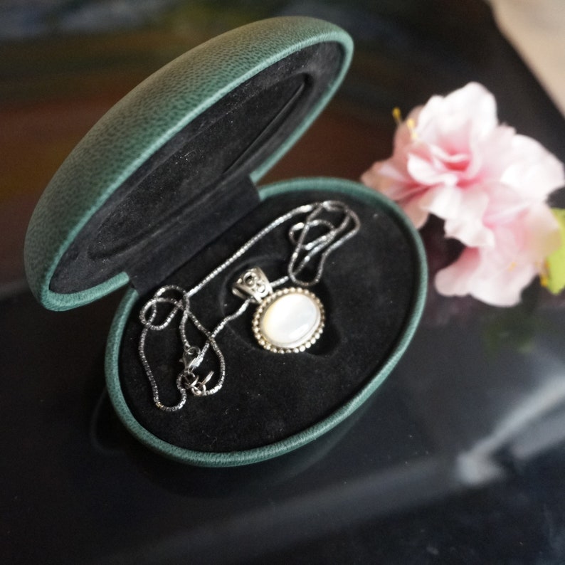 May include: A silver necklace with a white oval pendant in a green velvet jewelry box.