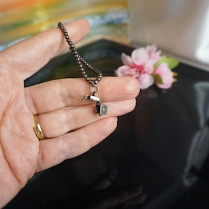 May include: A silver chain necklace with a small, open, silver box charm. The box is detailed with a textured design.