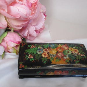May include: A black wooden box with a floral design painted on the lid. The flowers are in shades of red, yellow, orange, pink, and white. The box has a hinged lid and a small inscription on the front that reads "Mironga".