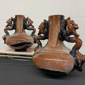 May include: Two brown and black ceramic vases with dragon handles. The vases have a mottled glaze and are decorated with a white and brown pattern.