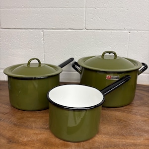 Peut inclure: Un ensemble de trois ustensiles de cuisine en émail vert olive avec des bords et des poignées noirs. La collection comprend une casserole avec couvercle, une marmite avec couvercle et une casserole ouverte. Chaque pièce a une finition brillante.