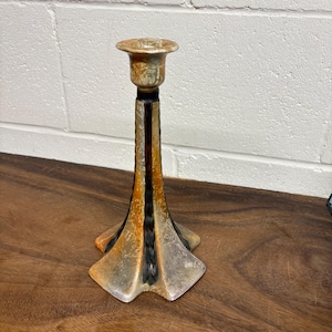 May include: A decorative candlestick holder with a flared base and a slender, vertical body. The candlestick is primarily gold and black, with a textured finish. The base is approximately 4 inches wide.