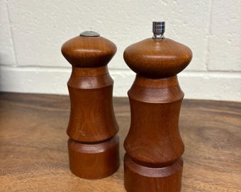 Può includere: Un paio di macinasale e pepe in legno. I macinini sono realizzati in legno marrone scuro con una finitura liscia. Un macinino ha la parte superiore argentata, l'altro ha la parte superiore piatta color argento. I macinini sono cilindrici con la parte superiore bulbosa.