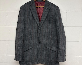 May include: A gray tweed blazer with a plaid pattern, hanging on a wooden hanger. The blazer has a burgundy lining and two front pockets. The jacket is buttoned and appears to be made of a wool blend.