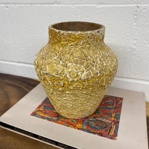 Peut inclure: Un vase en céramique jaune et blanc avec une surface texturée. Le vase a un corps arrondi et une large ouverture.