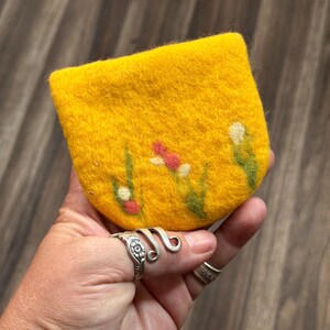May include: A small yellow felt coin purse with a floral design. The flowers are white, red, and green.