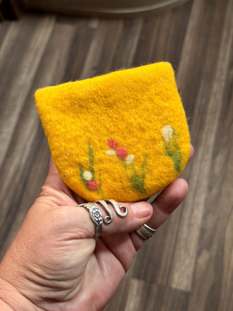 May include: A small yellow felt coin purse with a floral design. The flowers are white, red, and green.