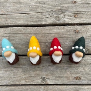 May include: Four felt gnome ornaments in different colors: blue, yellow, red, and green. Each gnome has a white beard and a white pom-pom hat with white dots.