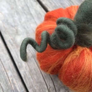 Op de afbeelding: Een handgevilte oranje en gele pompoen met een groene viltstengel. De stengel is gekruld en gedraaid.