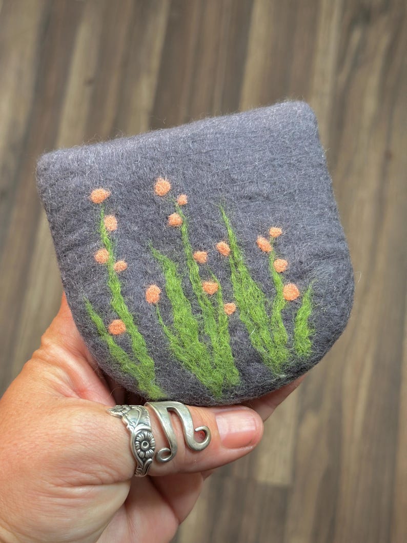 May include: A gray felt coin purse with a design of green leaves and orange flowers.