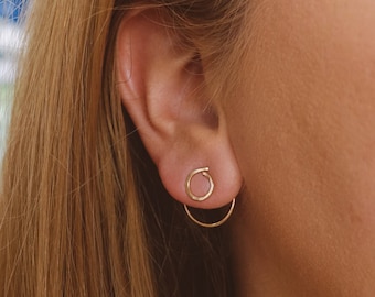 May include: A pair of gold hoop earrings with a smaller hoop attached to the larger hoop. The earrings are worn in the earlobe.