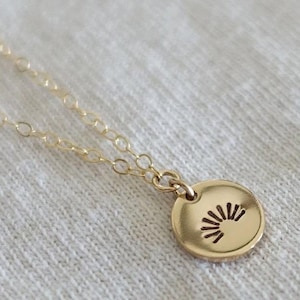 May include: A gold necklace with a small, round pendant featuring a sun design.