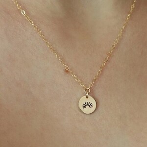 May include: A gold chain necklace with a small round pendant featuring a sun design.