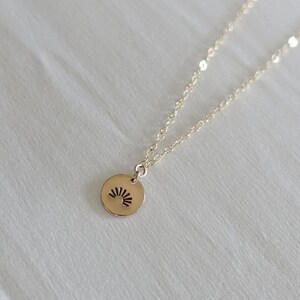 May include: A gold necklace with a small, round pendant featuring a sunburst design.
