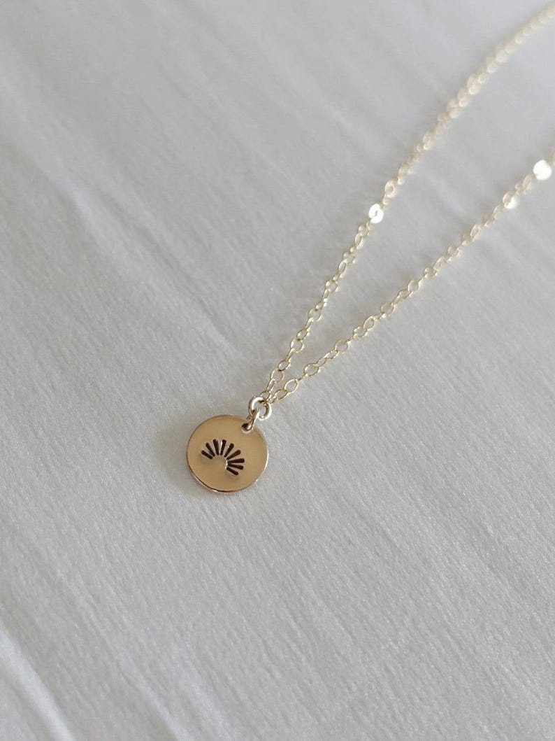 May include: A gold necklace with a small, round pendant featuring a sunburst design.
