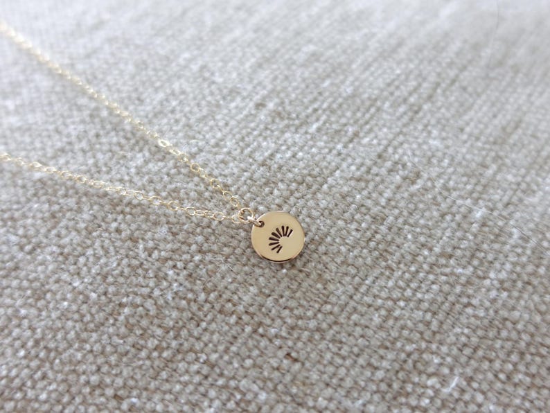 May include: A gold necklace with a small round pendant featuring a sun design.