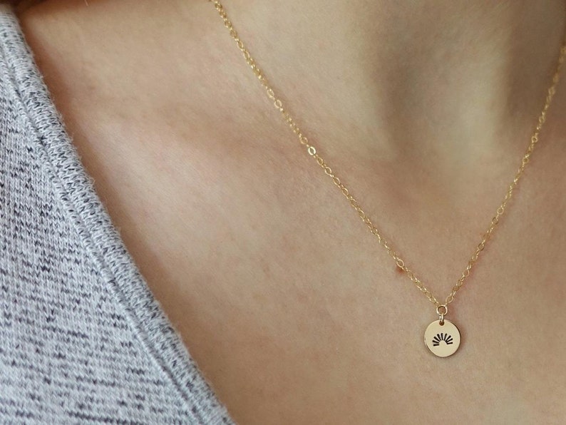 May include: A gold chain necklace with a small round pendant featuring a sun design.