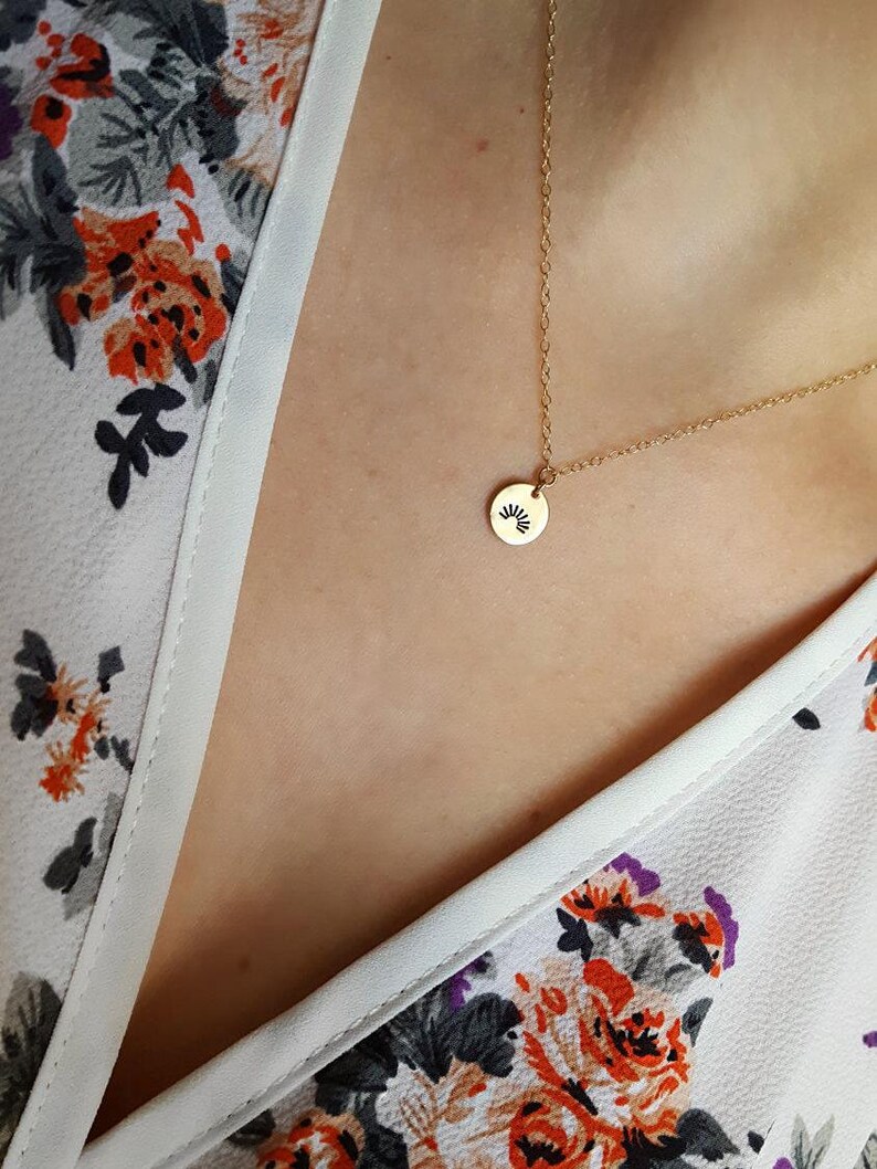 May include: A gold chain necklace with a small round pendant featuring a sunburst design.