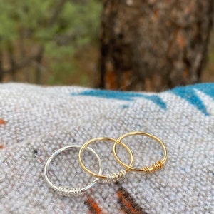 May include: Three simple wire rings, one silver and two gold, stacked on a patterned fabric background.