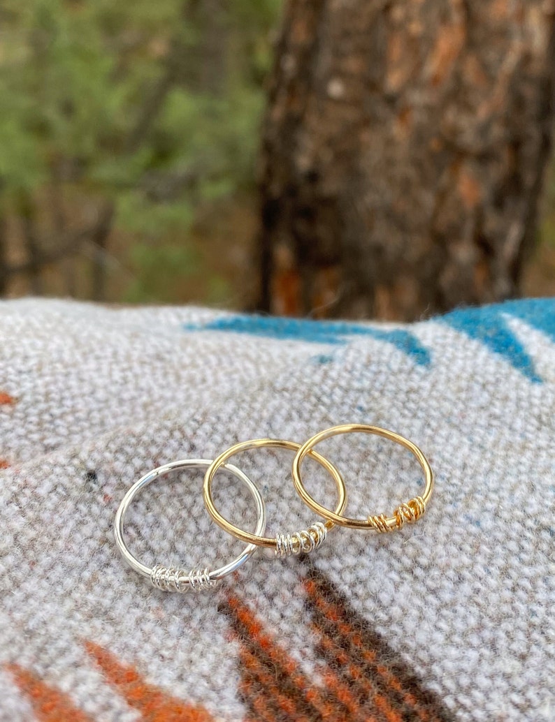 May include: Three simple wire rings, one silver and two gold, stacked on a patterned fabric background.