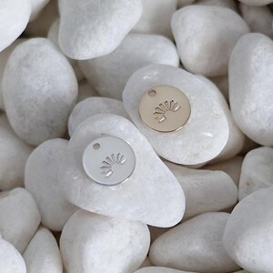 May include: Two small round metal charms with a sun design. One charm is silver and the other is gold.