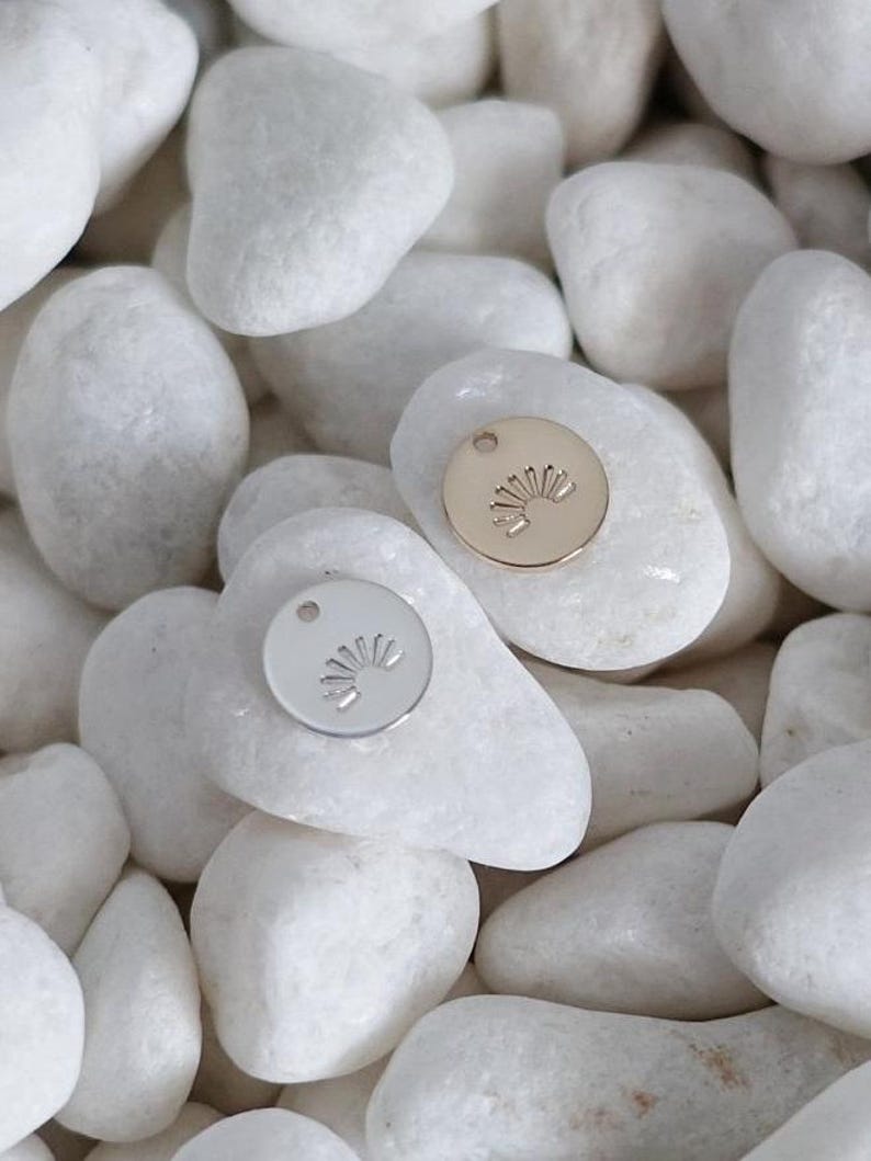 May include: Two small round metal charms with a sun design. One charm is silver and the other is gold.